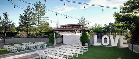 An outdoor wedding venue with white chairs arranged in rows, a stage with draped white fabric, and a large 'LOVE' sign.