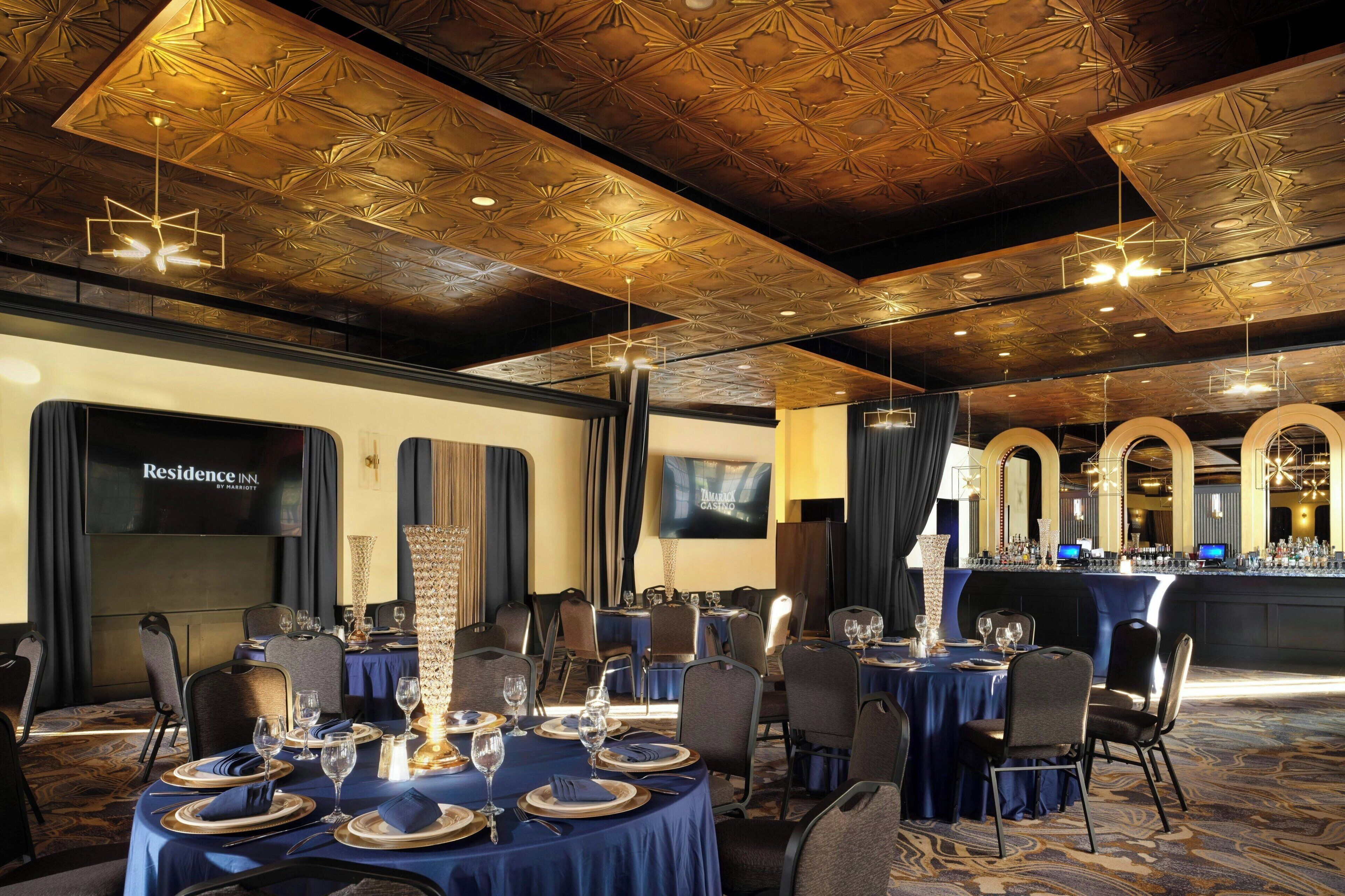 Un salón de banquetes con mesas redondas dispuestas para comer, una zona de bar y una pantalla de televisión que muestra 