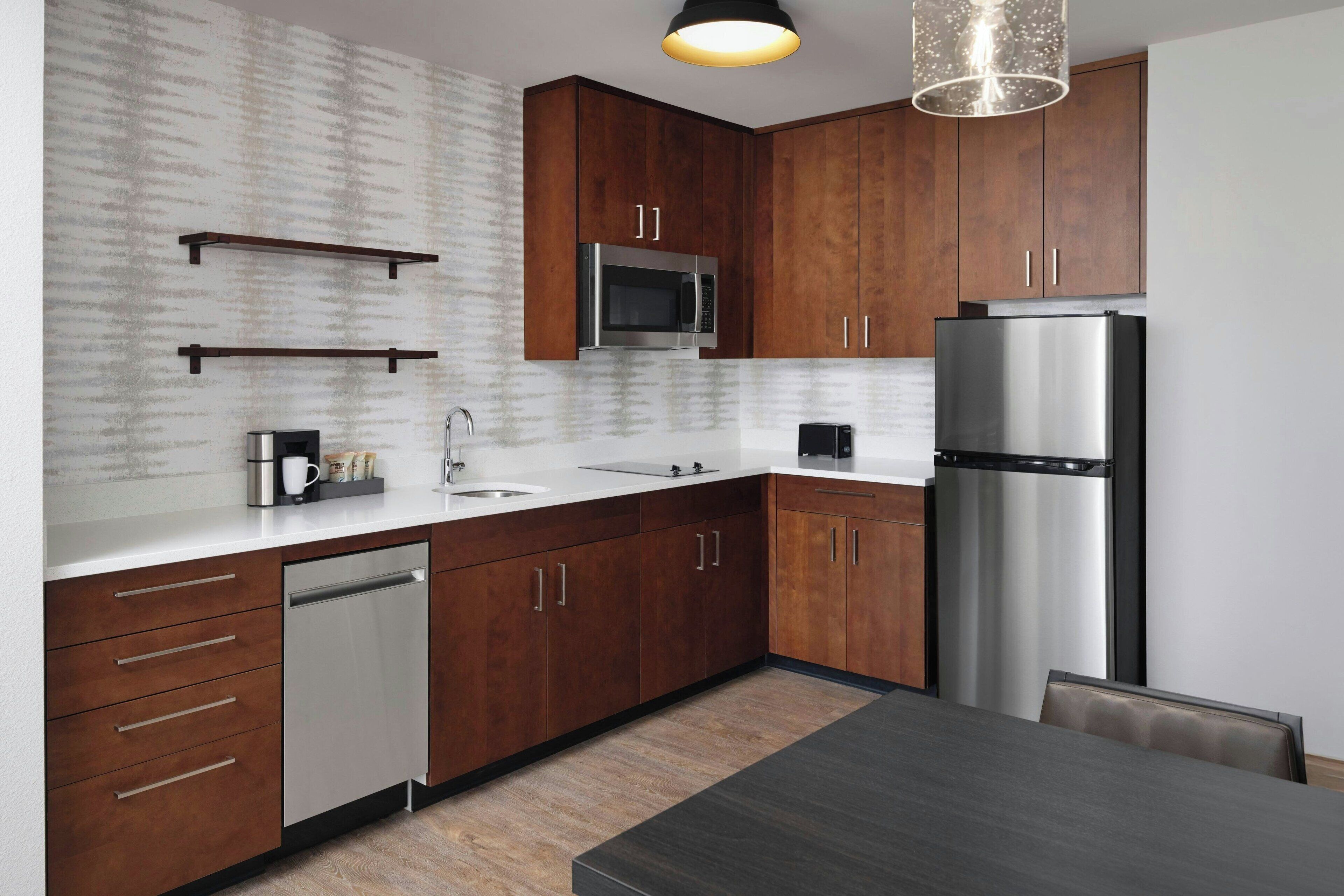 A modern kitchen with wooden cabinets, stainless steel appliances, and a dining area with a dark table.