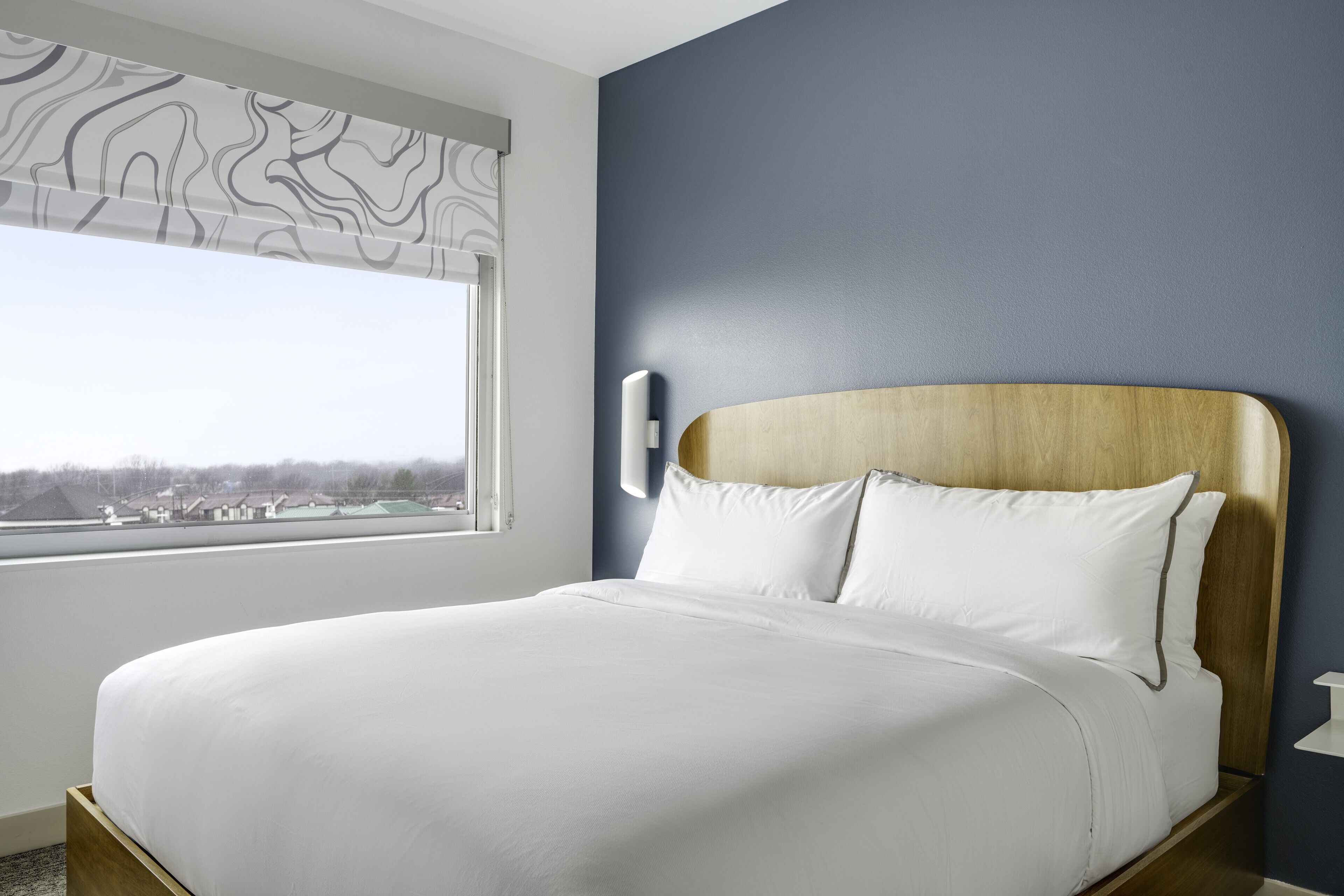 Una cama bien hecha con sábanas blancas en una habitación con vistas a la ciudad a través de una ventana.
