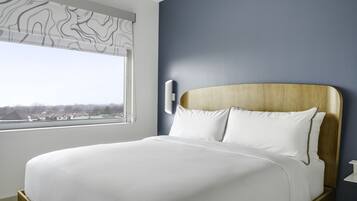Una cama bien hecha con sábanas blancas en una habitación con vistas a la ciudad a través de una ventana.