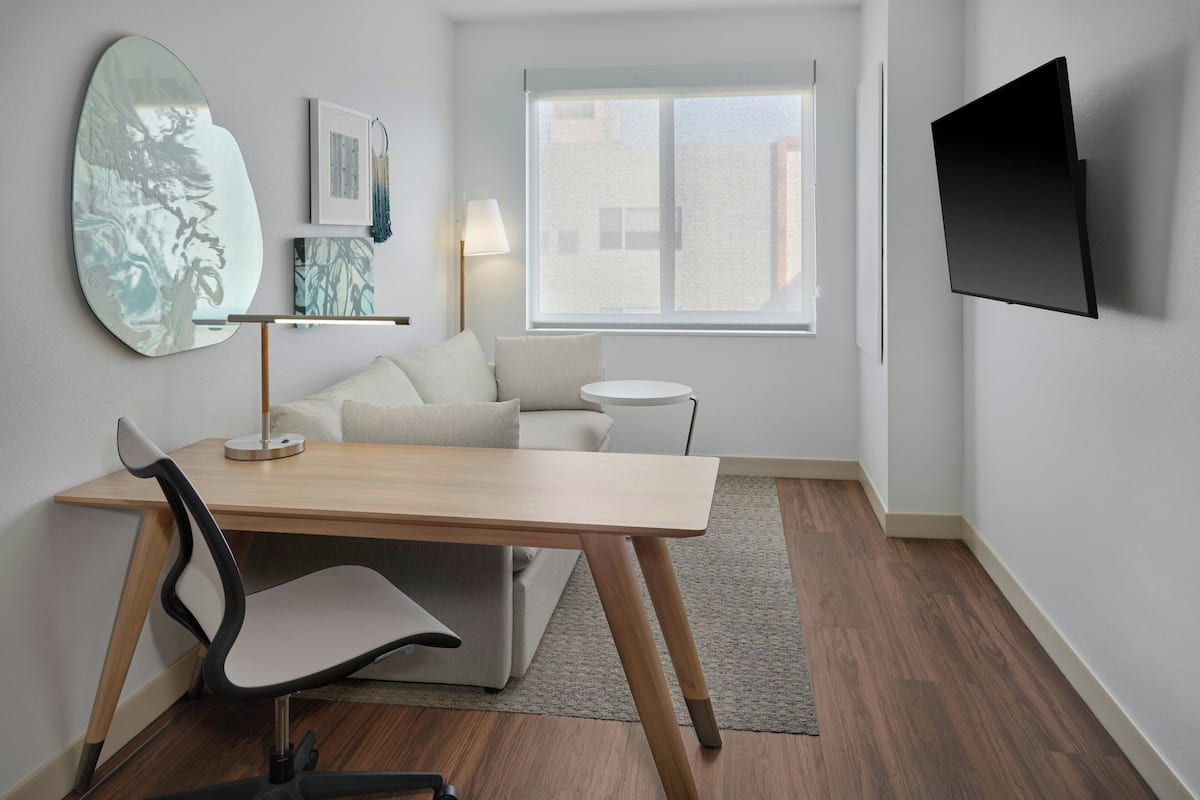 A modern room with a wooden desk, a white chair, a sofa, a round side table, and a mounted TV.