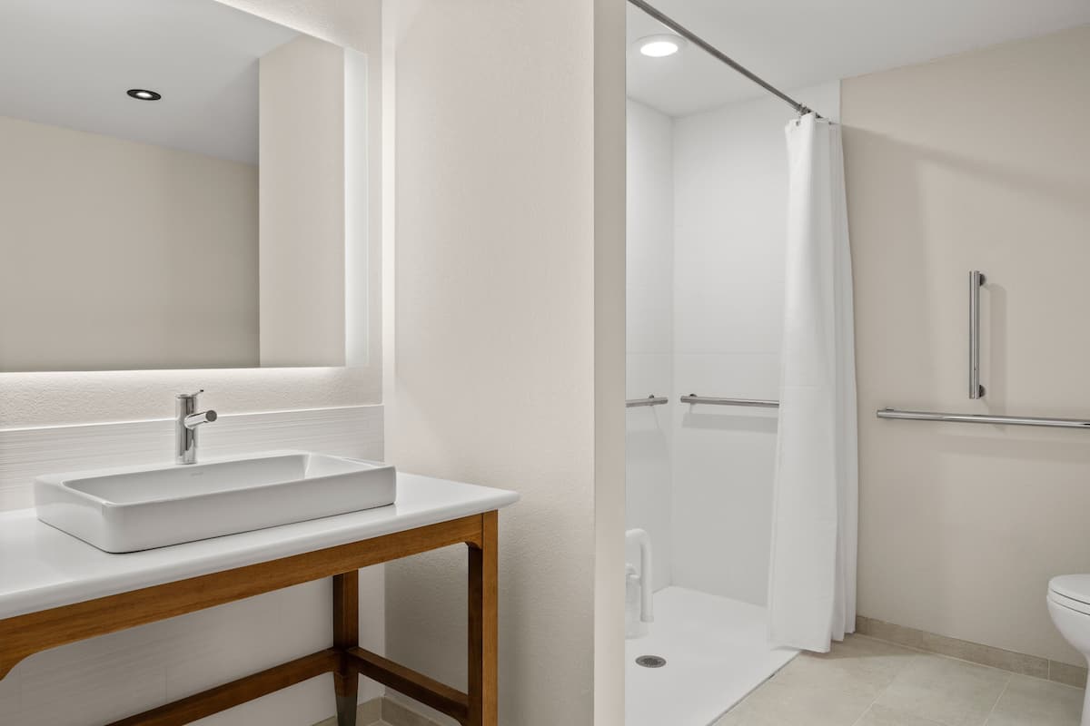 A modern bathroom with a white sink, wooden vanity, and a glass-enclosed shower.