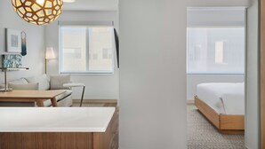 A modern hotel room with a large bed, a desk, a chair, a lamp, and a decorative light fixture.