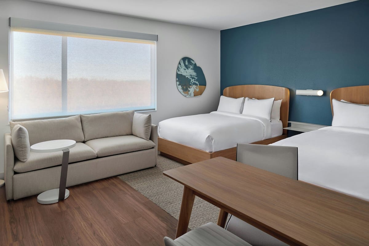 A hotel room with a bed, a sofa, a small table, and a wall-mounted artwork.