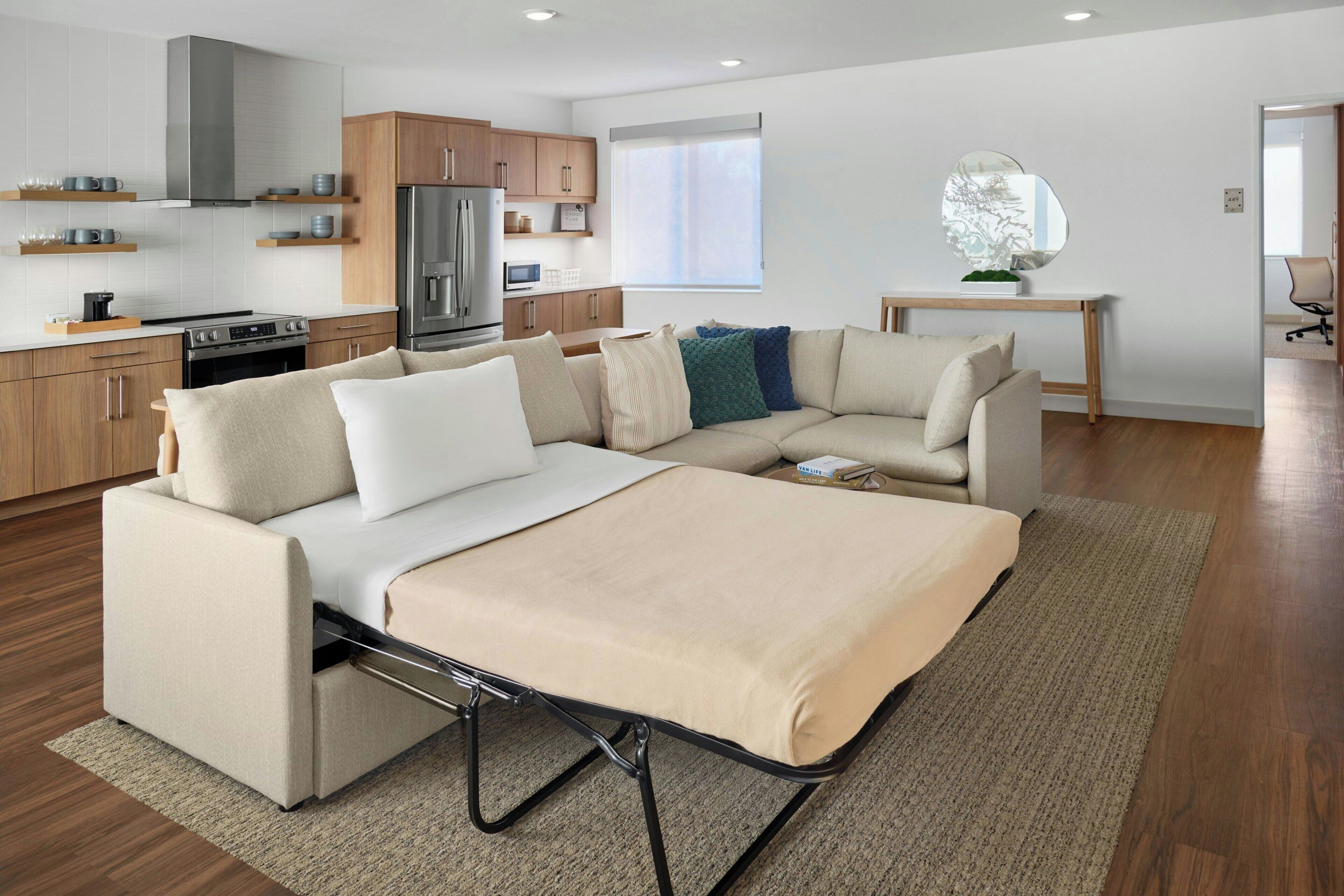 Un espacio habitable moderno con sofá cama, zona de cocina y mesa de comedor.
