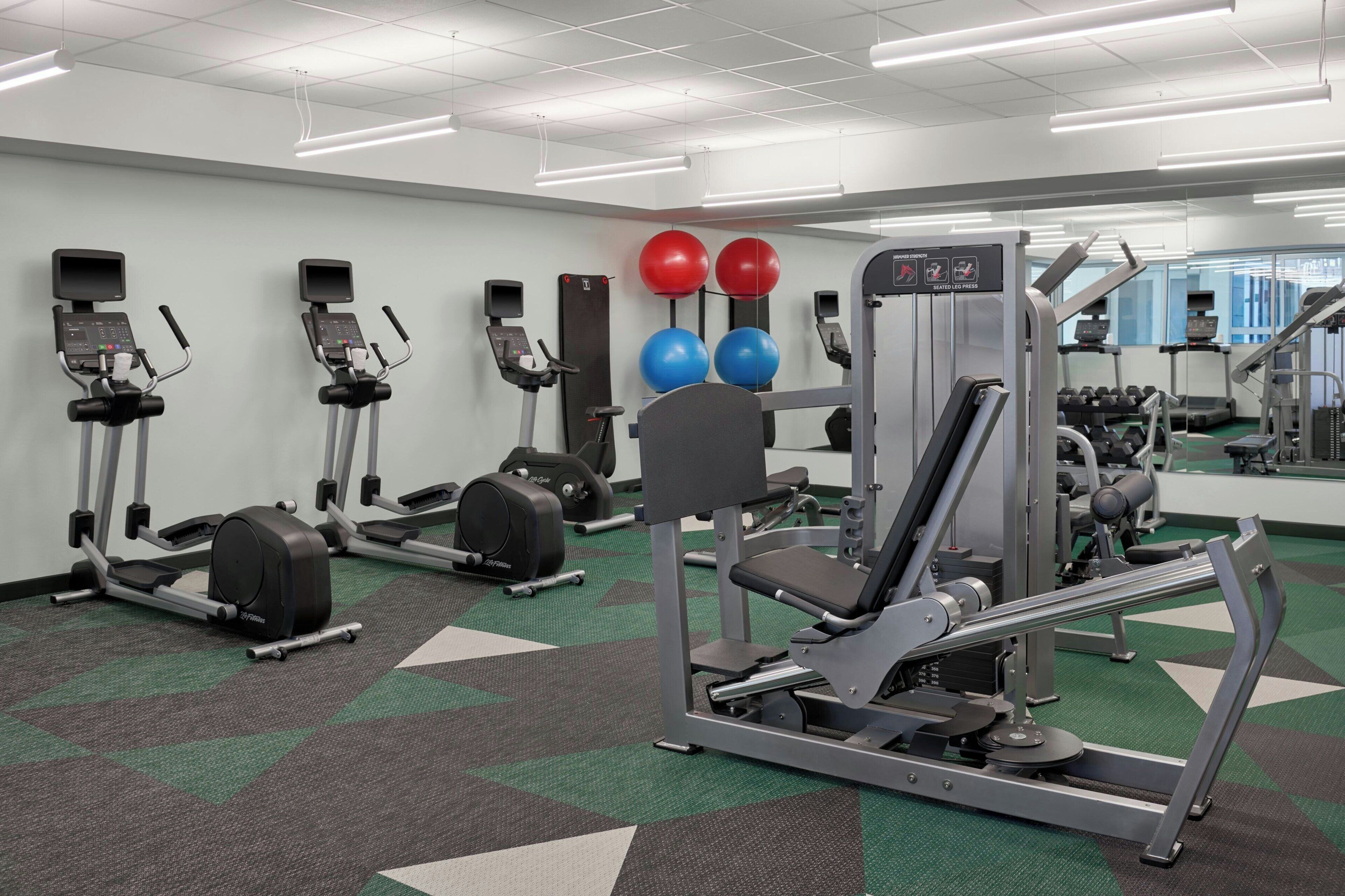 A gym with treadmills, ellipticals, a weight machine, and exercise balls.