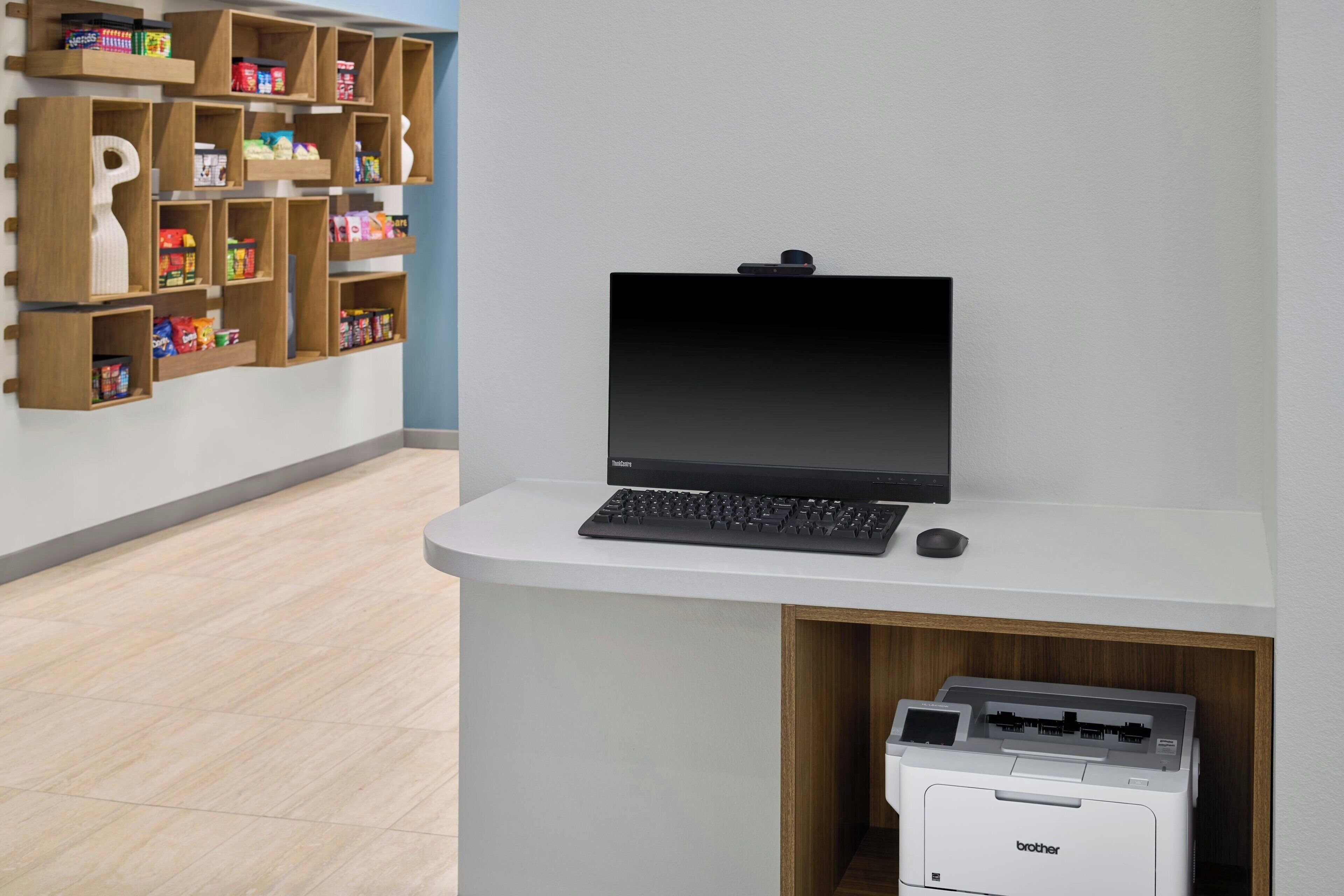 A reception desk with a laptop, a printer, and a keyboard. There is a wooden shelf unit with various items on the wall behind the desk.