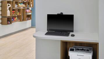 A reception desk with a laptop, a printer, and a keyboard. There is a wooden shelf unit with various items on the wall behind the desk.