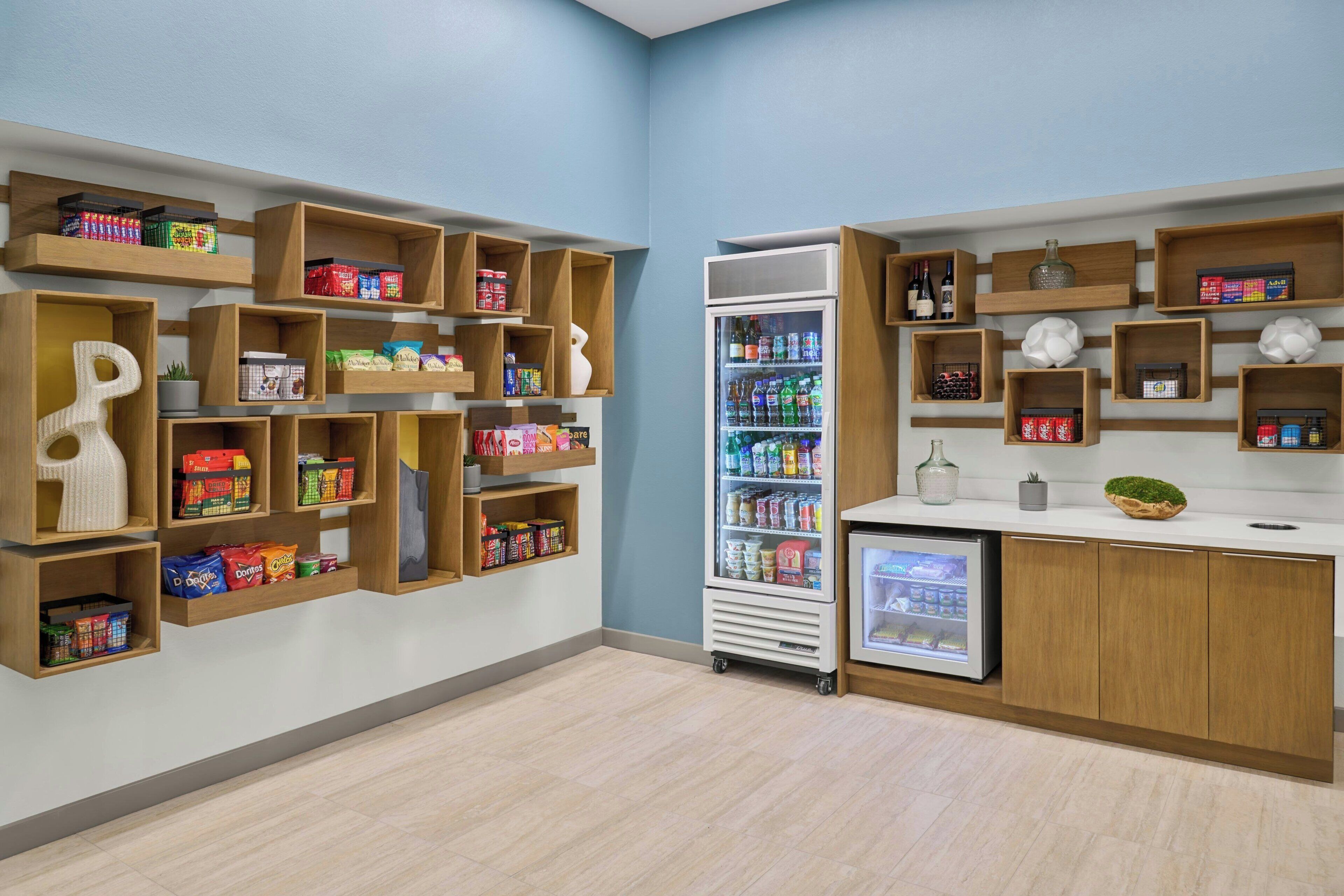 A modern retail space with wooden shelves stocked with snacks and beverages, a refrigerated display, and a small counter with a decorative bowl.