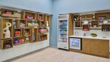 A modern retail space with wooden shelves stocked with snacks and beverages, a refrigerated display, and a small counter with a decorative bowl.