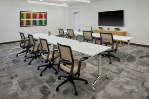 A conference room with a long table, multiple chairs, a TV screen, and a colorful abstract painting on the wall.