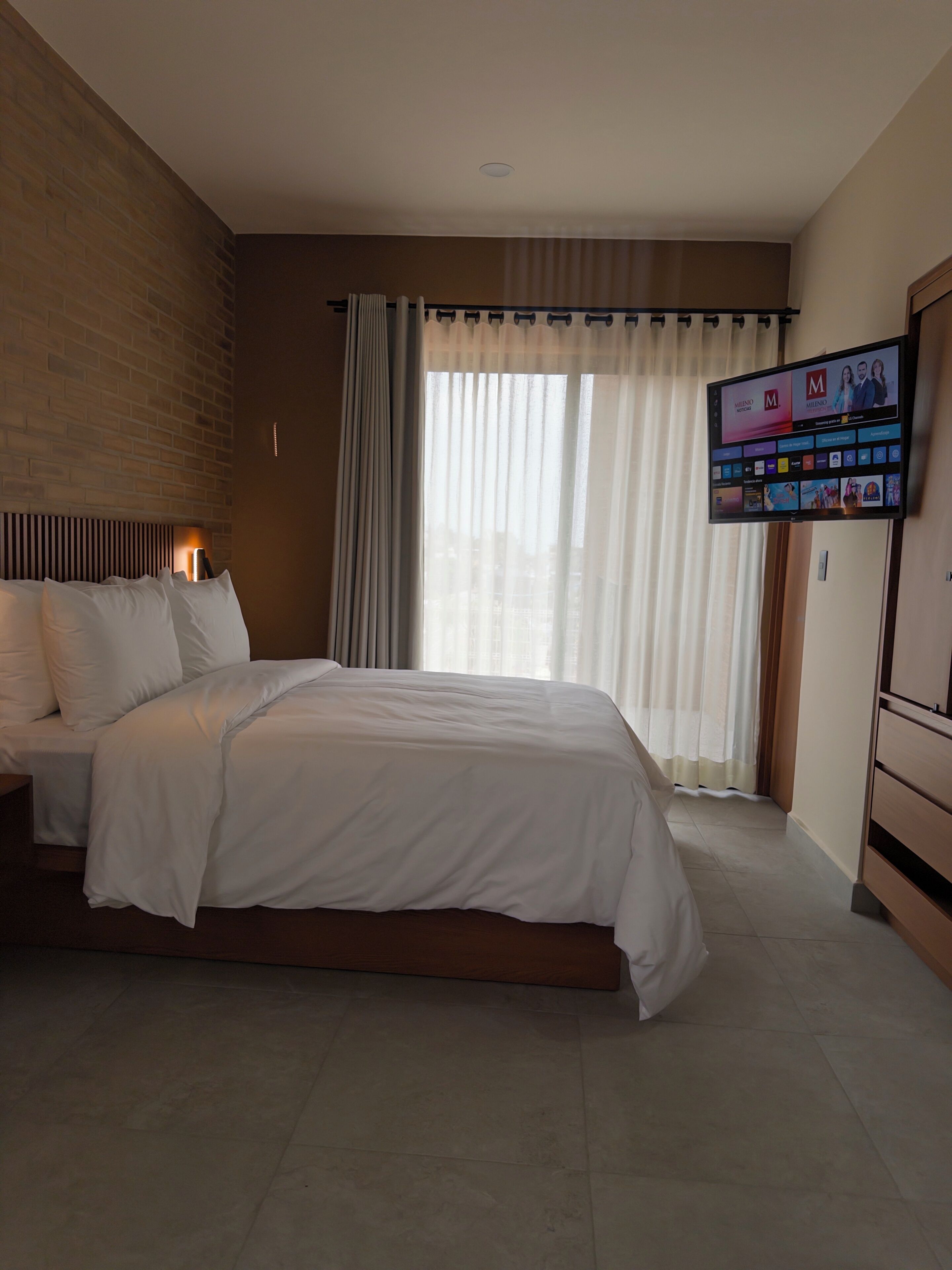 Une chambre d’hôtel avec un grand lit, un téléviseur fixé au mur et une fenêtre avec des rideaux.