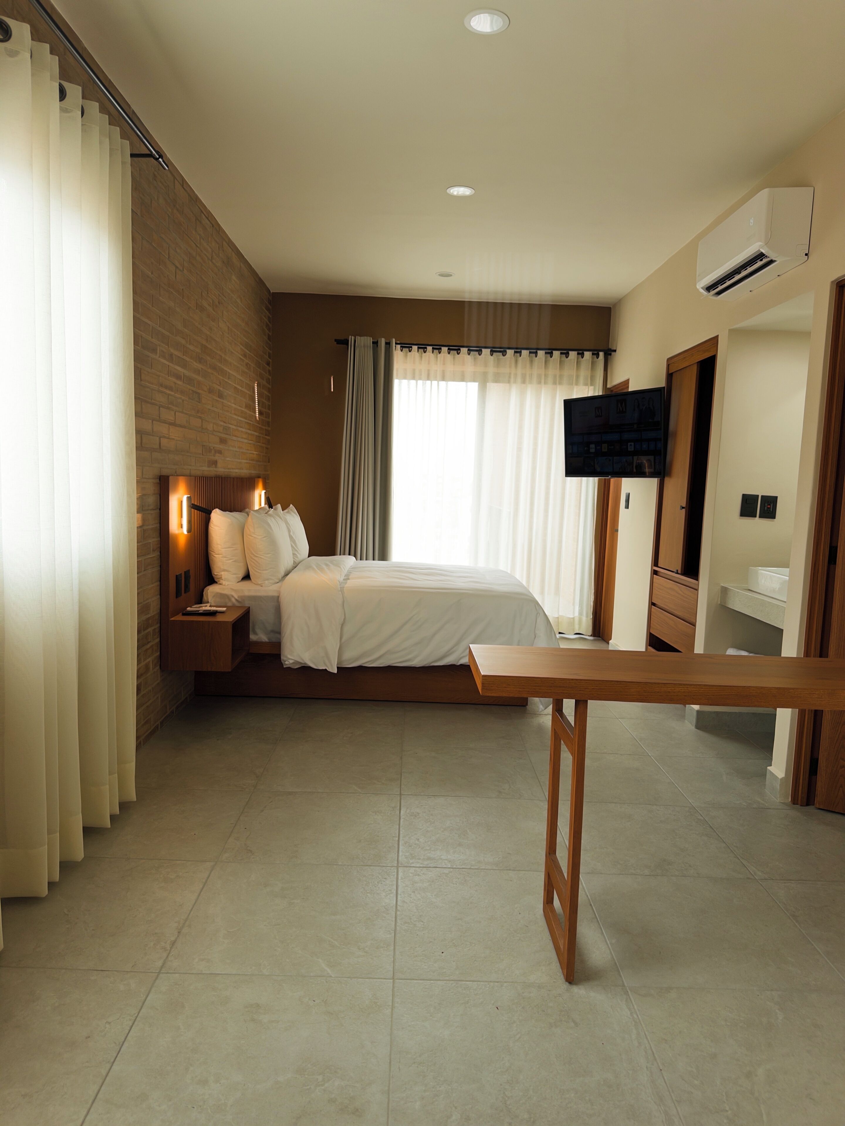 Un dormitorio de hotel moderno con cama, mesitas de noche, televisor y un banco de madera.