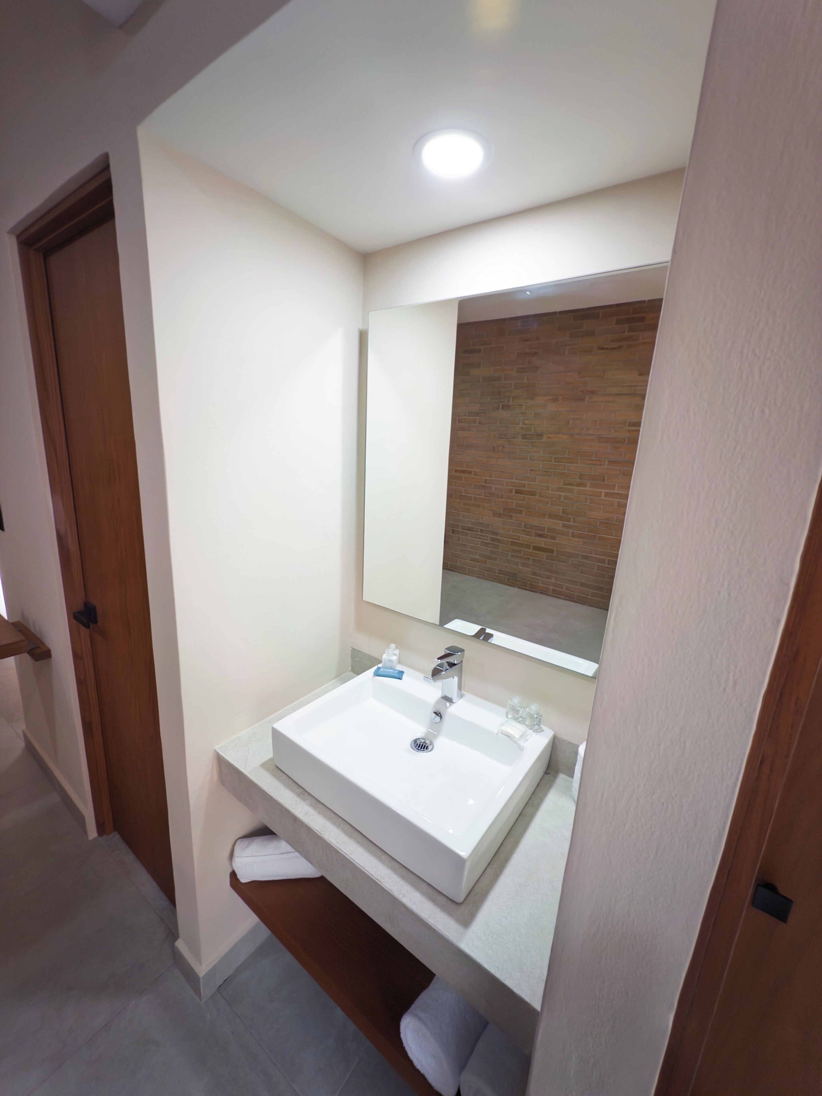 A modern bathroom with a white sink, a mirror, and a wooden door.