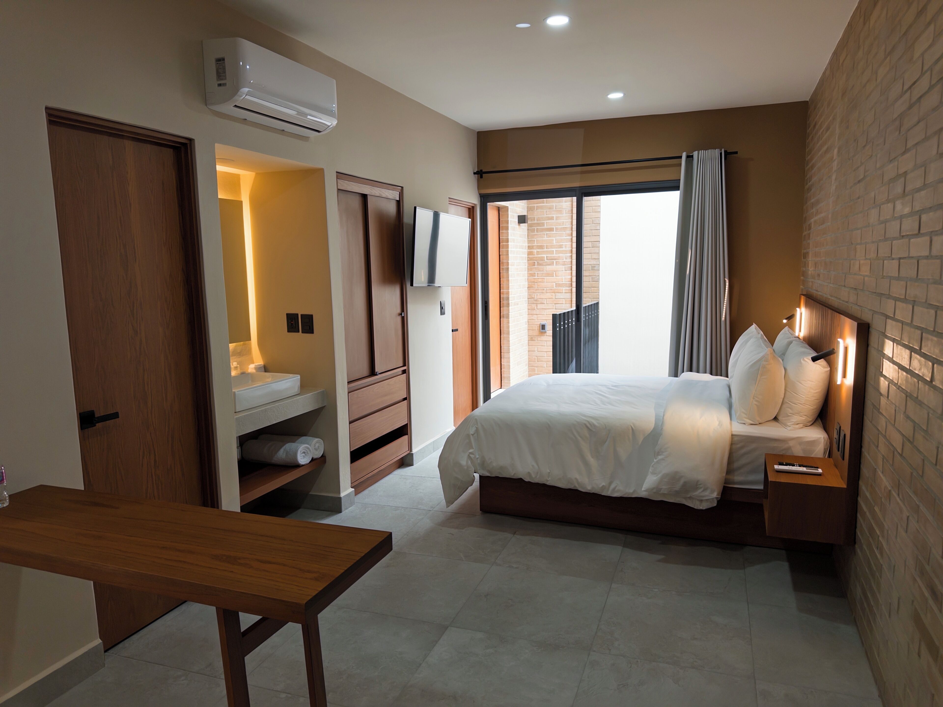 Quarto moderno com cama, mesa de cabeceira e escrivaninha de madeira.