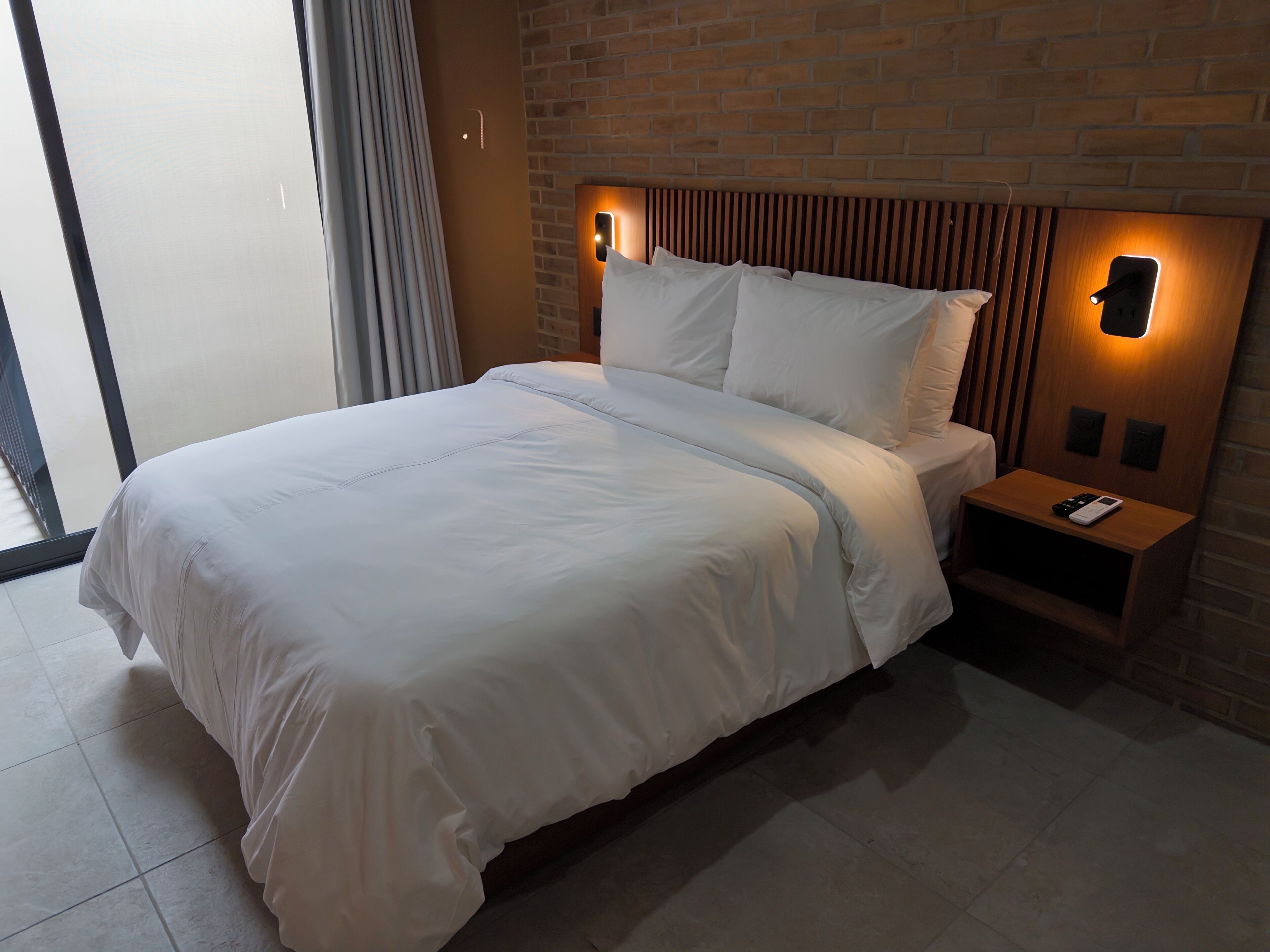 A modern hotel room with a large bed, a nightstand with a phone, and a brick wall.