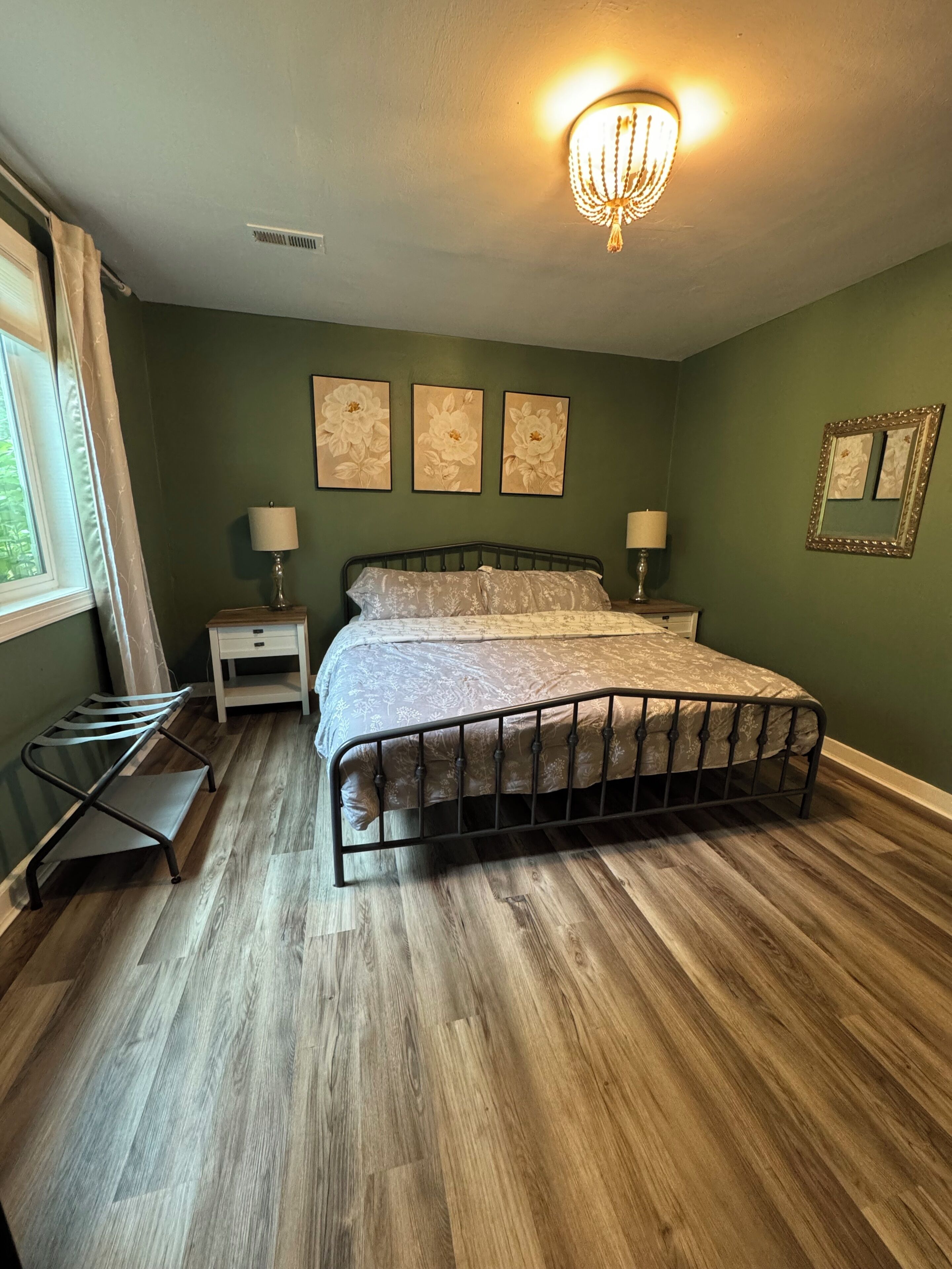 Quarto com uma cama, duas mesas de cabeceira com abajures, uma janela com cortinas e três quadros de flores na parede.