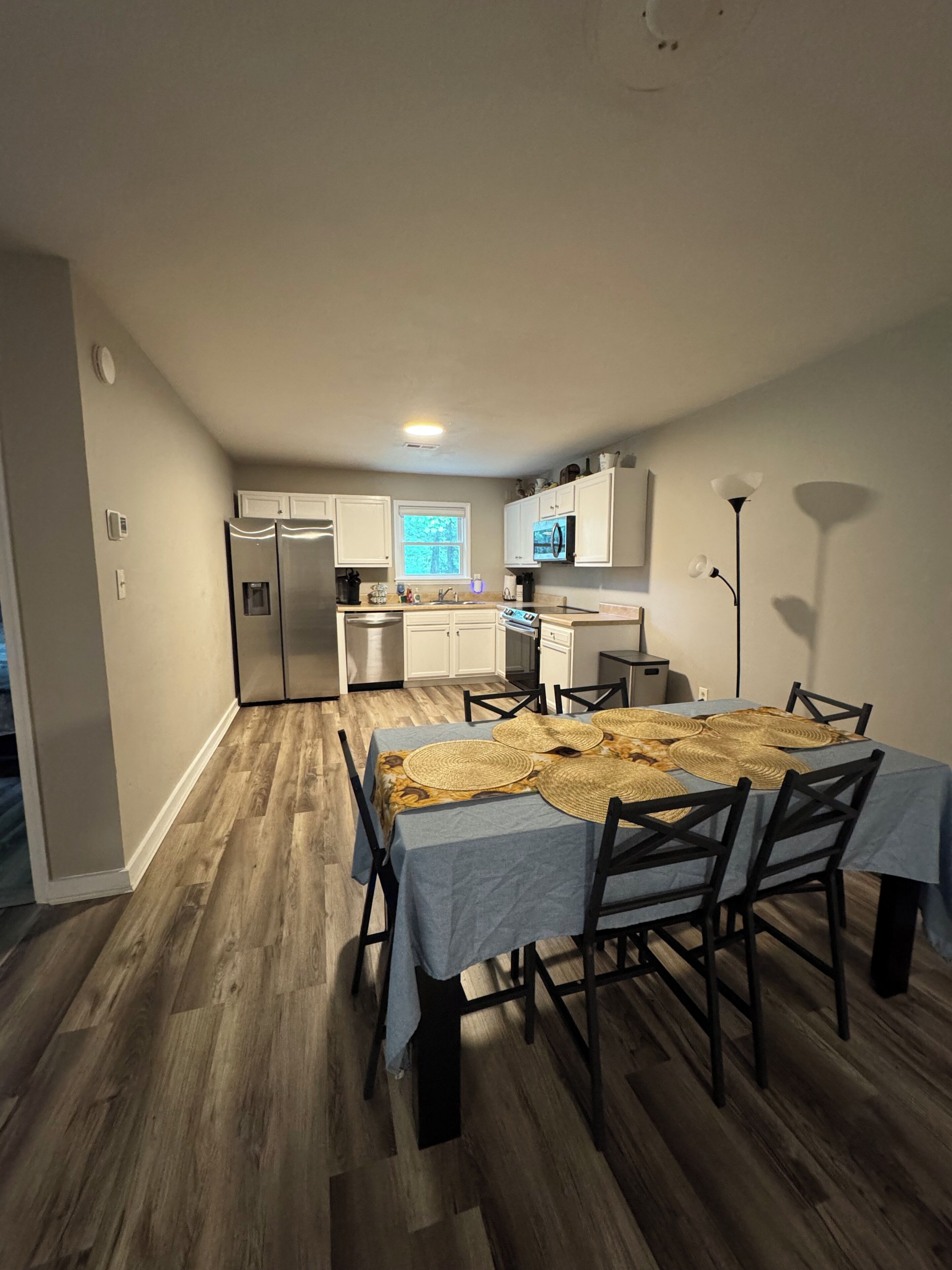 Un comedor con una mesa dispuesta para cuatro personas, una cocina al fondo y una lámpara en el techo.