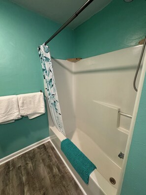 A bathroom with teal walls, a white bathtub, and a shower area.