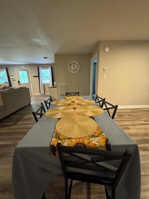 A dining area with a long table, chairs, a clock on the wall, and a view of the outdoors through large windows. - Escape to Comfort in Newport (Newport)