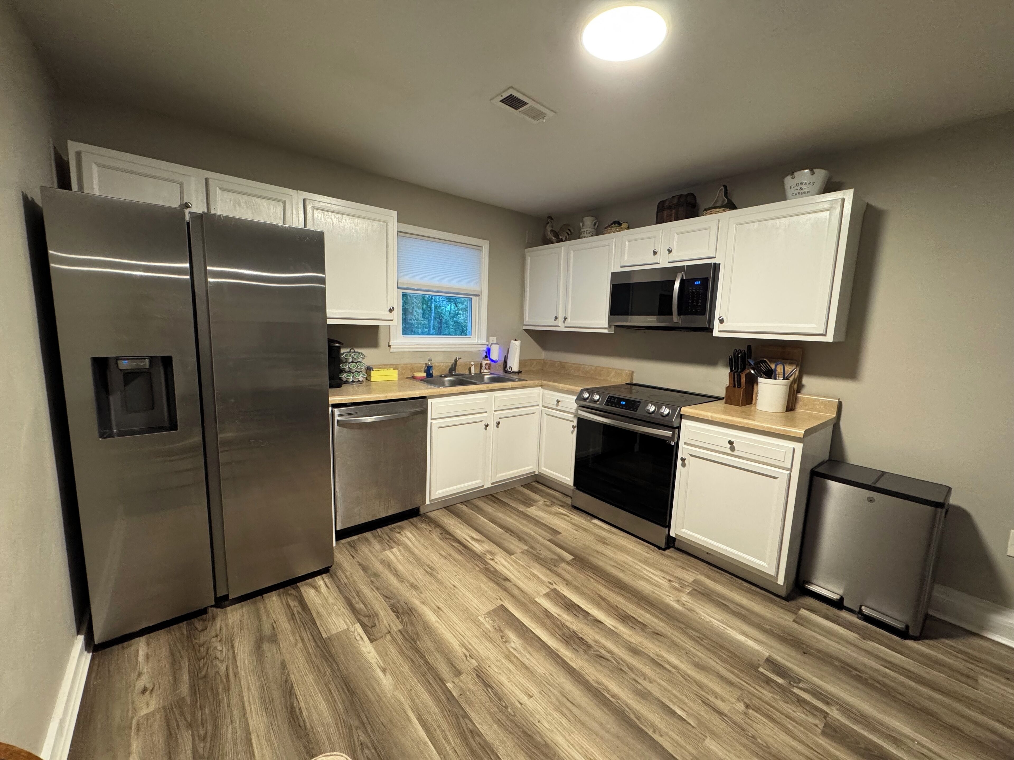 A modern kitchen with stainless steel appliances, white cabinetry, and a wooden floor.
