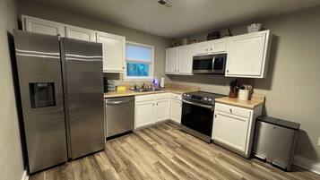 A modern kitchen with stainless steel appliances, white cabinetry, and a wooden floor.