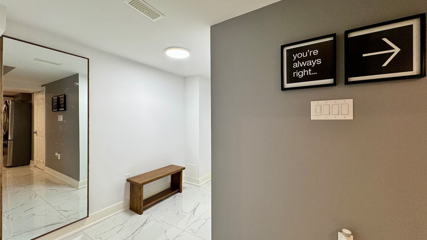A hallway with a mirror, a wooden bench, and two signs on the wall.