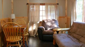 A cozy room with a wooden ceiling, a sofa, a chair, and a table. - Polar Bear Cabin at The Bears Cottages (Inlet)