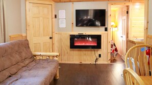 A cozy room with a wooden ceiling, a flat-screen TV mounted above a fireplace, a wooden bench, and a wooden chair. - Polar Bear Cabin at The Bears Cottages (Inlet)