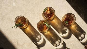 Three glasses of amber liquid with rosemary sprigs, placed on a textured surface with shadows.