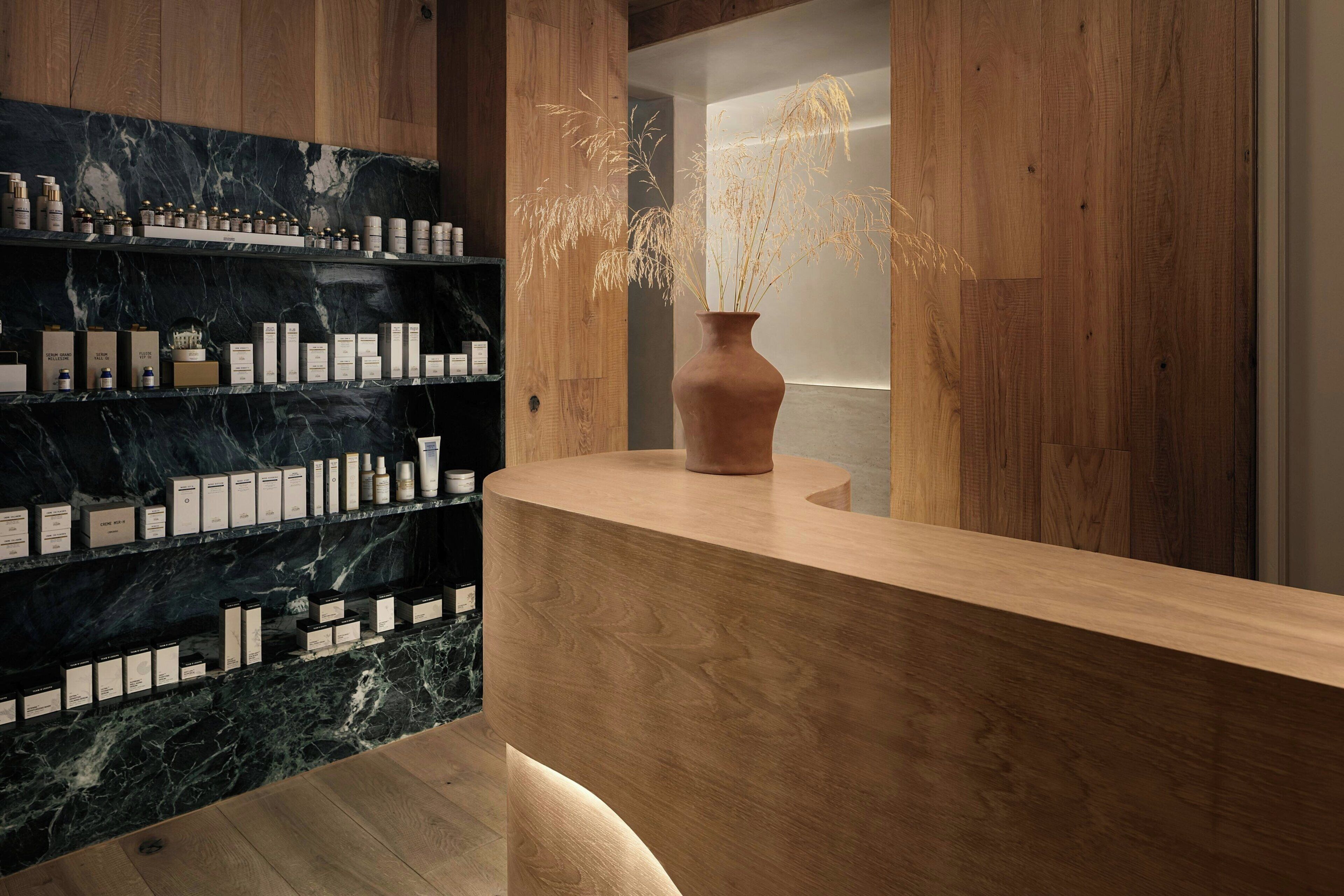 A reception area with a wooden reception desk, marble shelves with product displays, and a vase with dried plants.