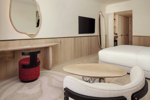 A modern hotel room with a round wooden table, a red ottoman, a white sofa, and a large mirror on the wall. - Morea House, Autograph Collection (Camps Bay)