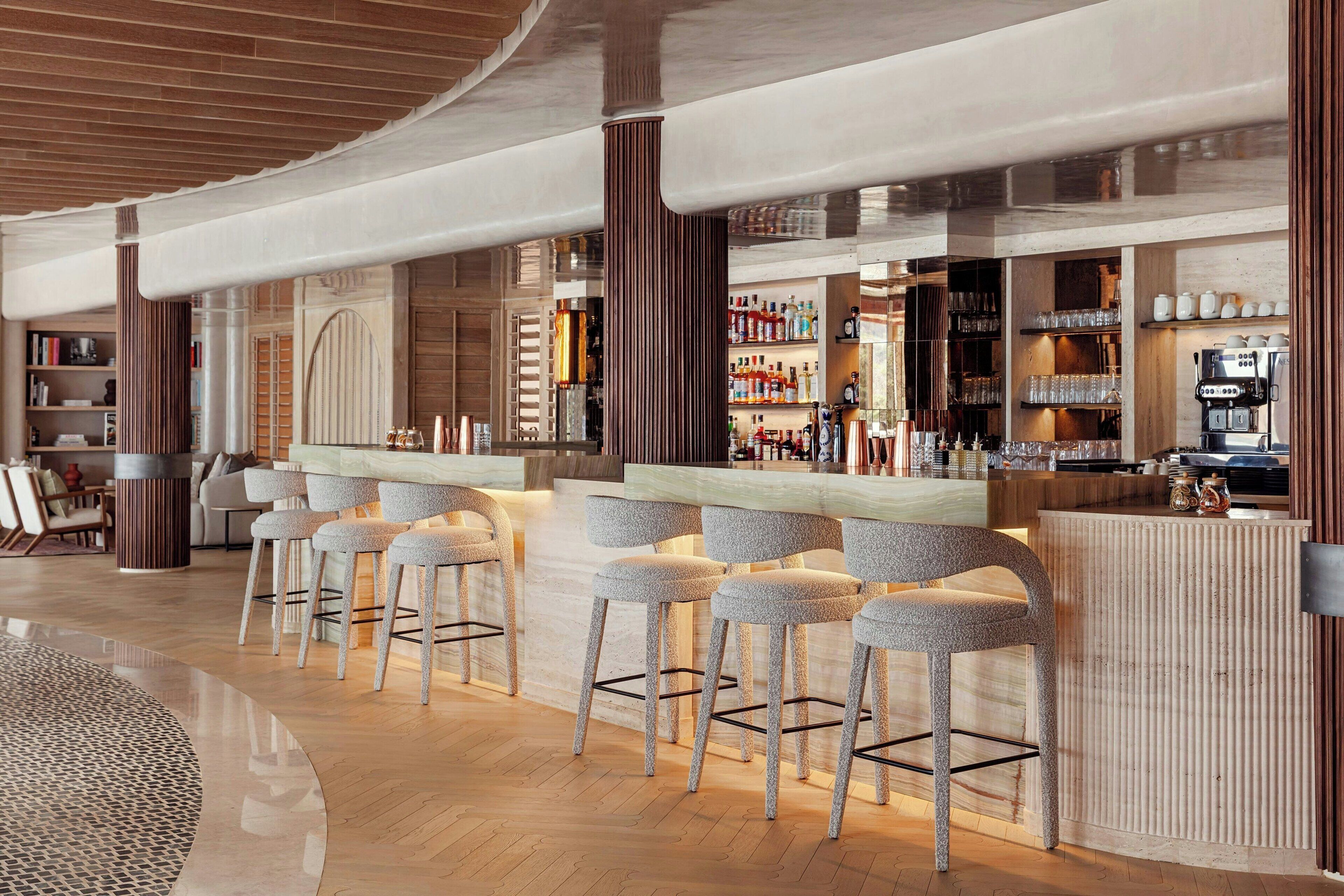 A modern bar area with high stools, a wooden counter, and a variety of bottles and glasses.