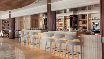A modern bar area with high stools, a wooden counter, and a variety of bottles and glasses.