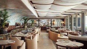 Un restaurant spacieux avec de hauts plafonds, de grandes fenêtres et différents types de sièges, notamment des banquettes et des tables rondes.