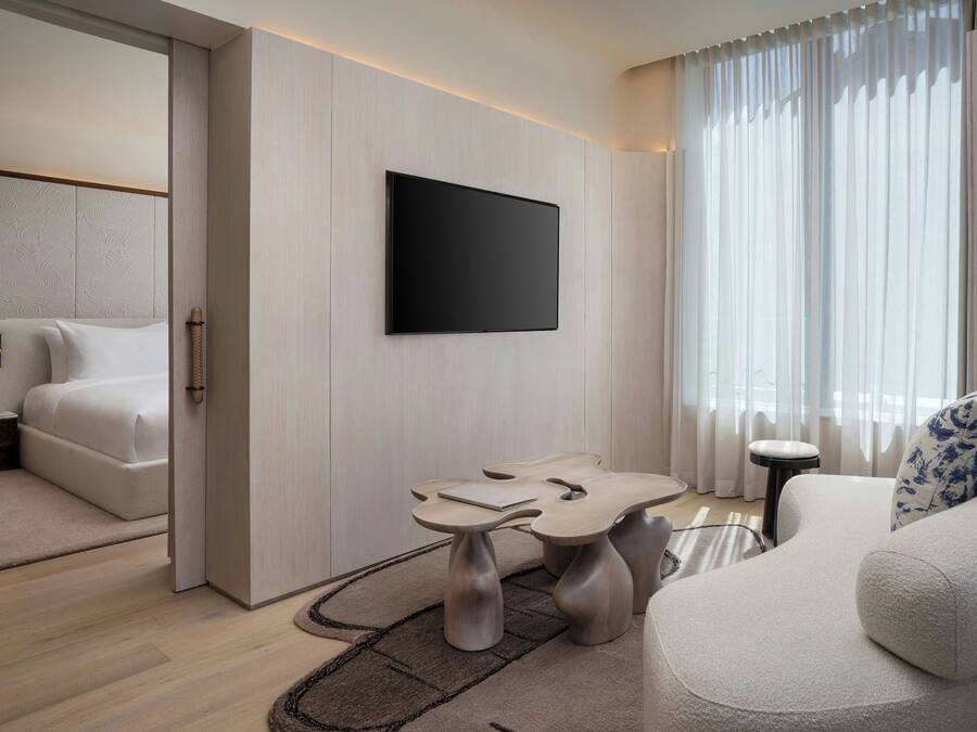 A modern hotel room with a bed, a flat-screen TV mounted on the wall, a small table, and a sofa.