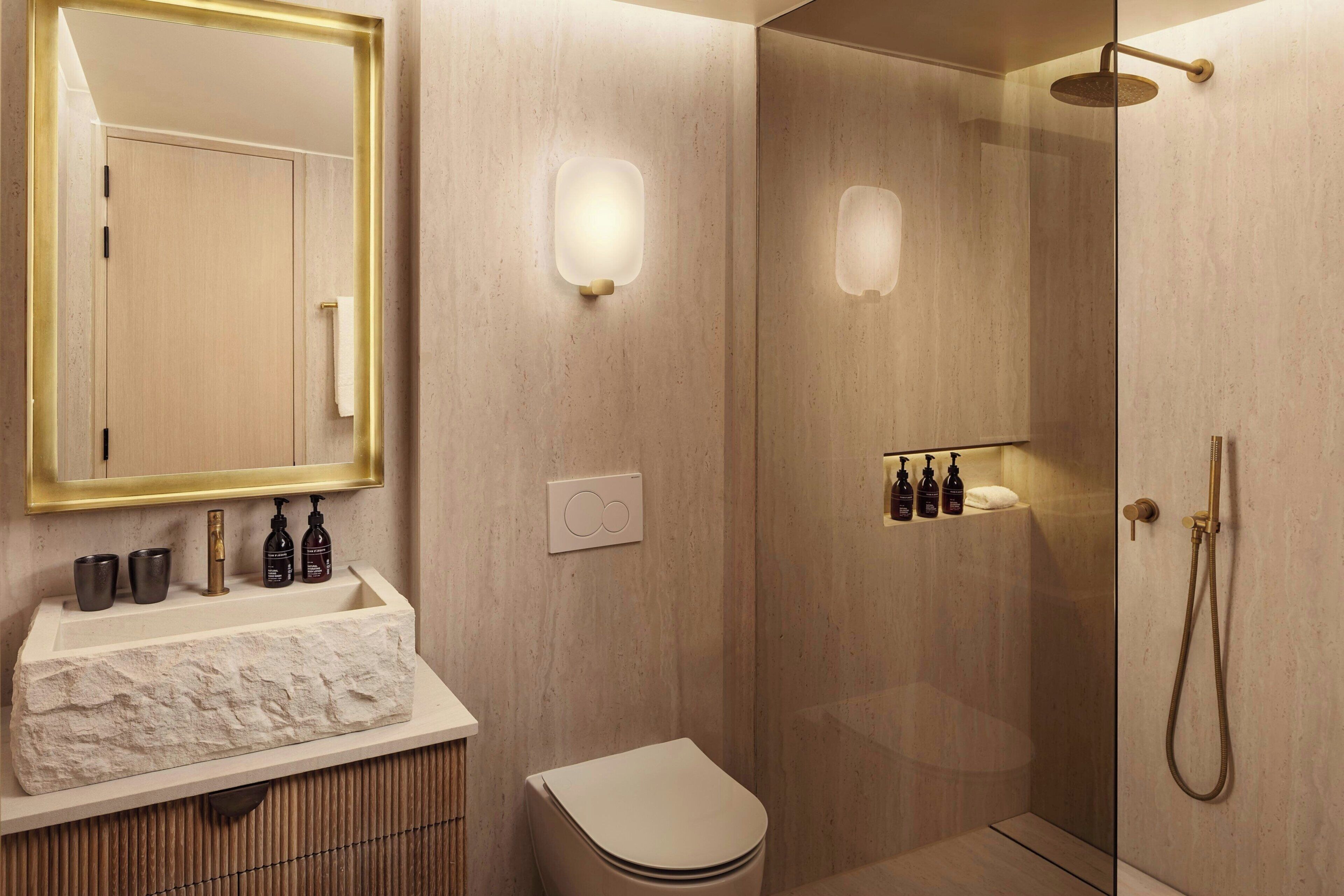 A modern bathroom with a glass-enclosed shower, a white sink with a marble countertop, and a mirror with a gold frame.