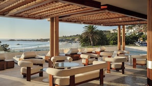 Un espace extérieur aménagé, abrité et doté de canapés et de tables, offrant une vue sur une plage et l’océan.