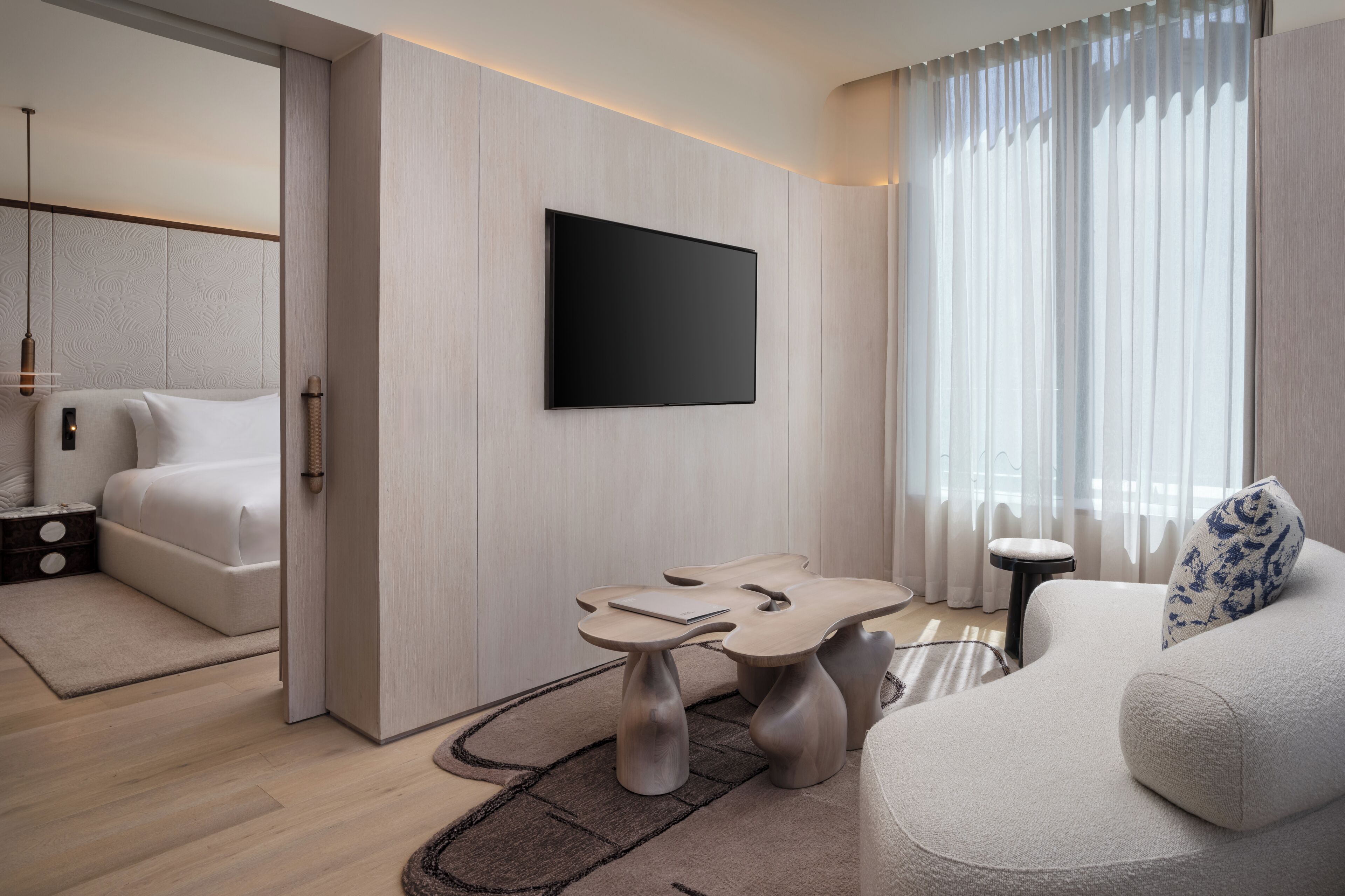 A modern hotel room with a bed, a flat-screen TV, a sofa, and a small table.