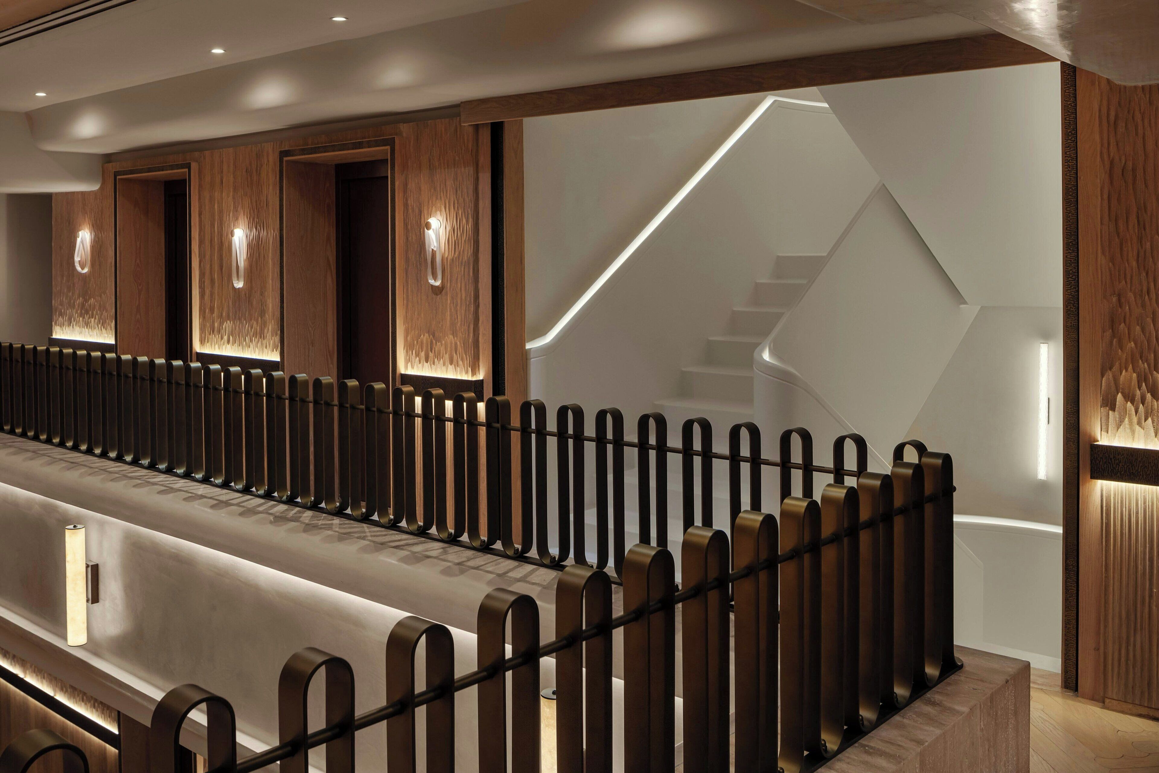 A modern hotel lobby with a long reception desk, wooden paneling, and a staircase with a geometric design.