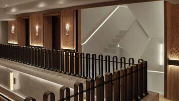A modern hotel lobby with a long reception desk, wooden paneling, and a staircase with a geometric design.