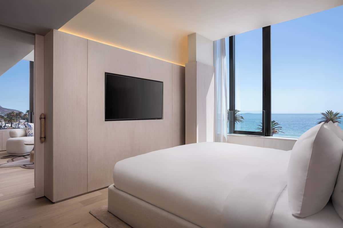 A modern bedroom with a large bed, a flat-screen TV, and a view of the ocean.