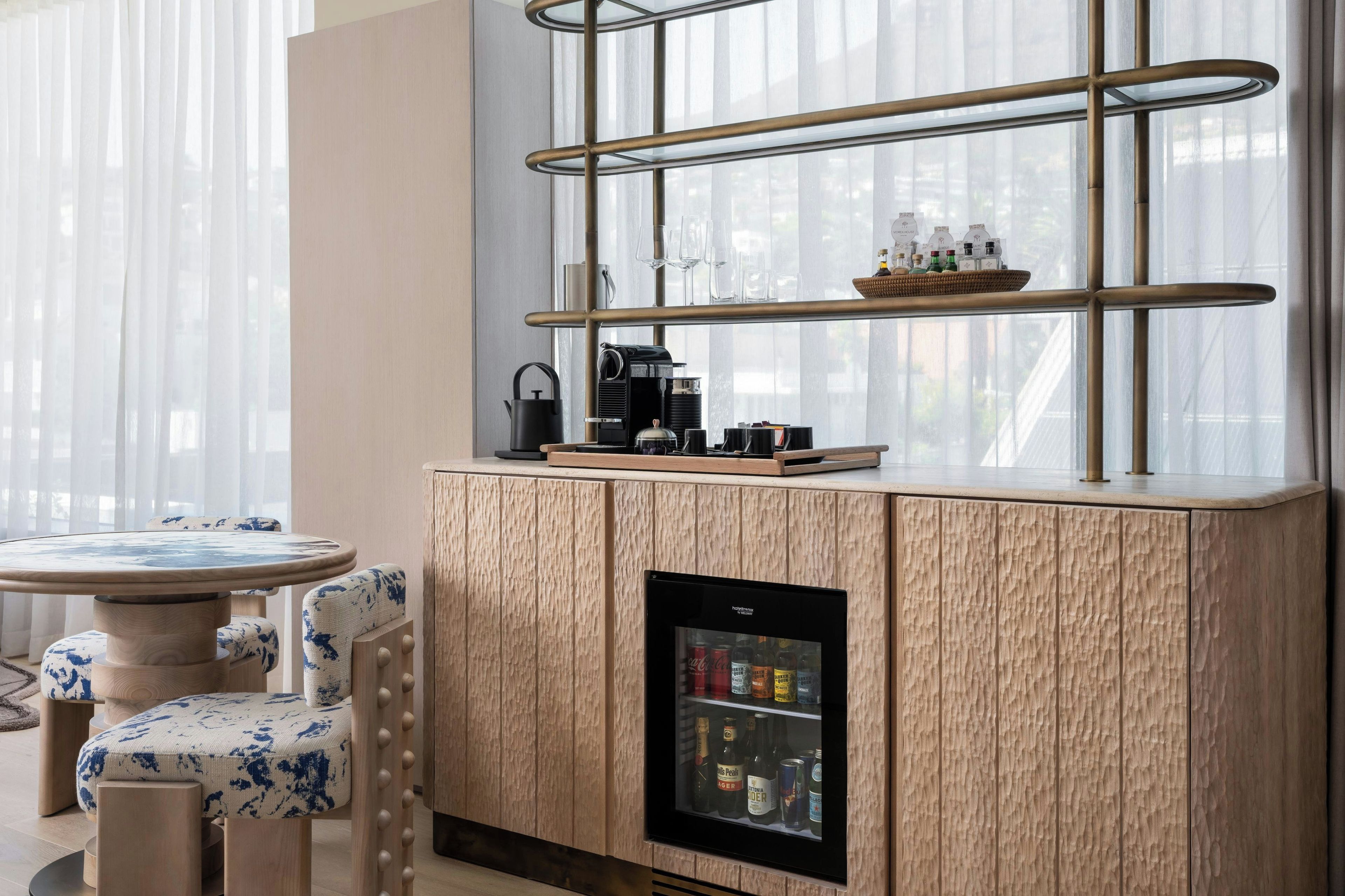 A modern kitchenette with a built-in coffee machine, a mini-fridge, and a glass shelf with bottles.