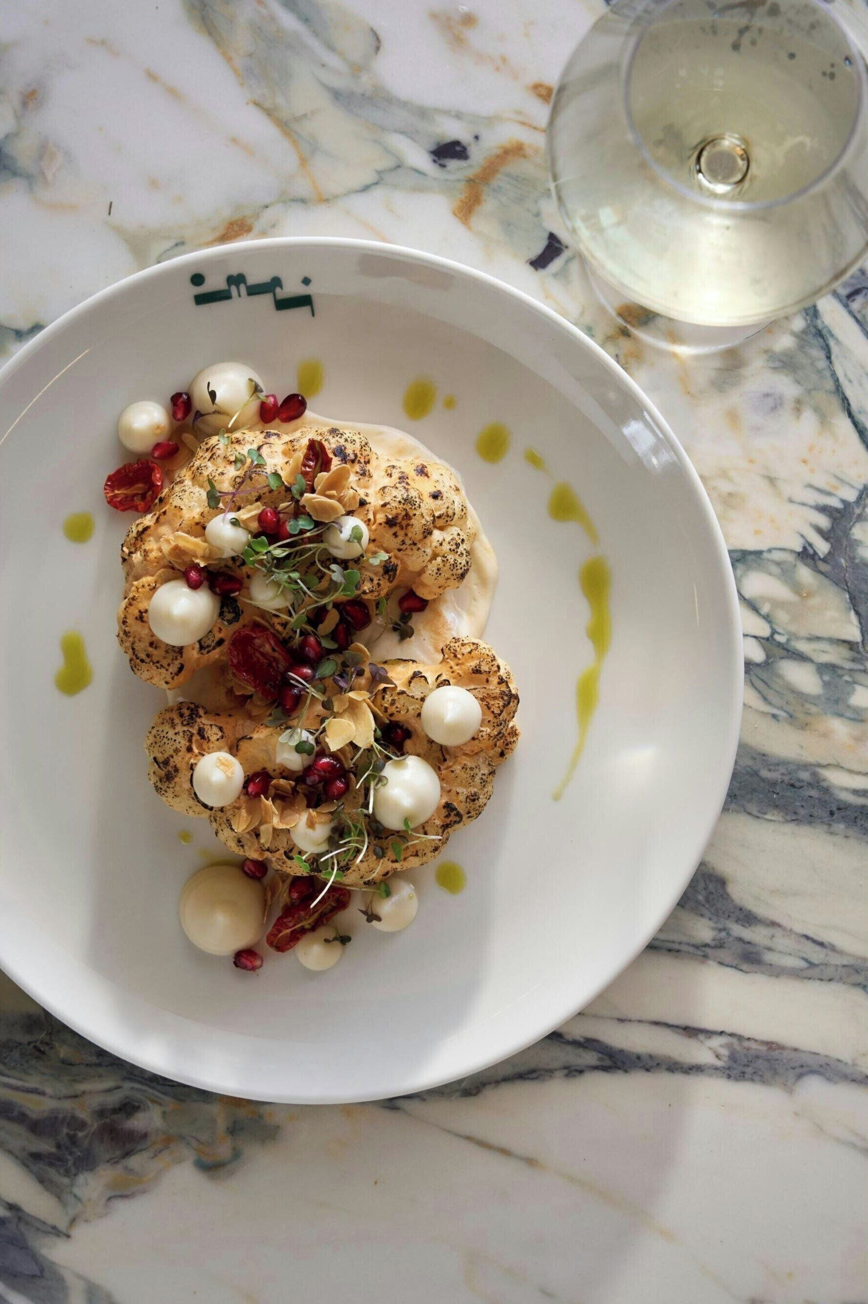 A white plate with a food dish, garnished with pomegranate seeds and microgreens, on a marble surface.