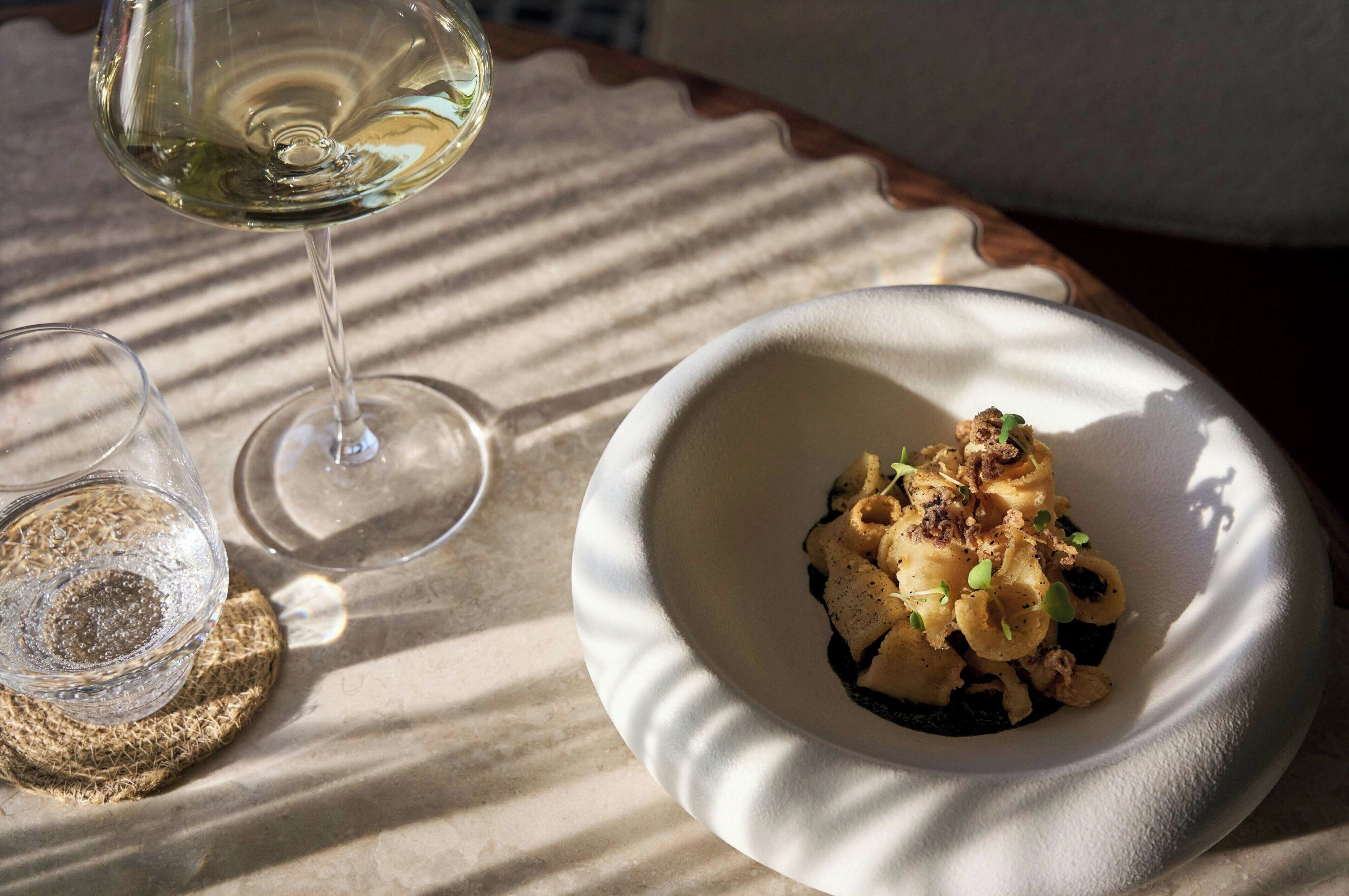 Une table avec un verre de vin blanc, un verre avec une paille et un bol de pâtes garni.