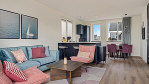 A modern living room with a sofa, coffee table, and chairs, a kitchen area with bar stools, and a dining table with chairs. - WW | Dijkhuys Buitenbubbelbad (Opperdoes)
