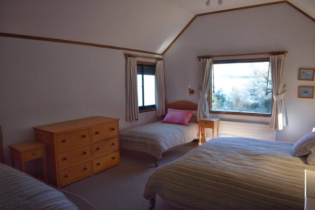 A bedroom with two beds, a wooden dresser, and a window with curtains.