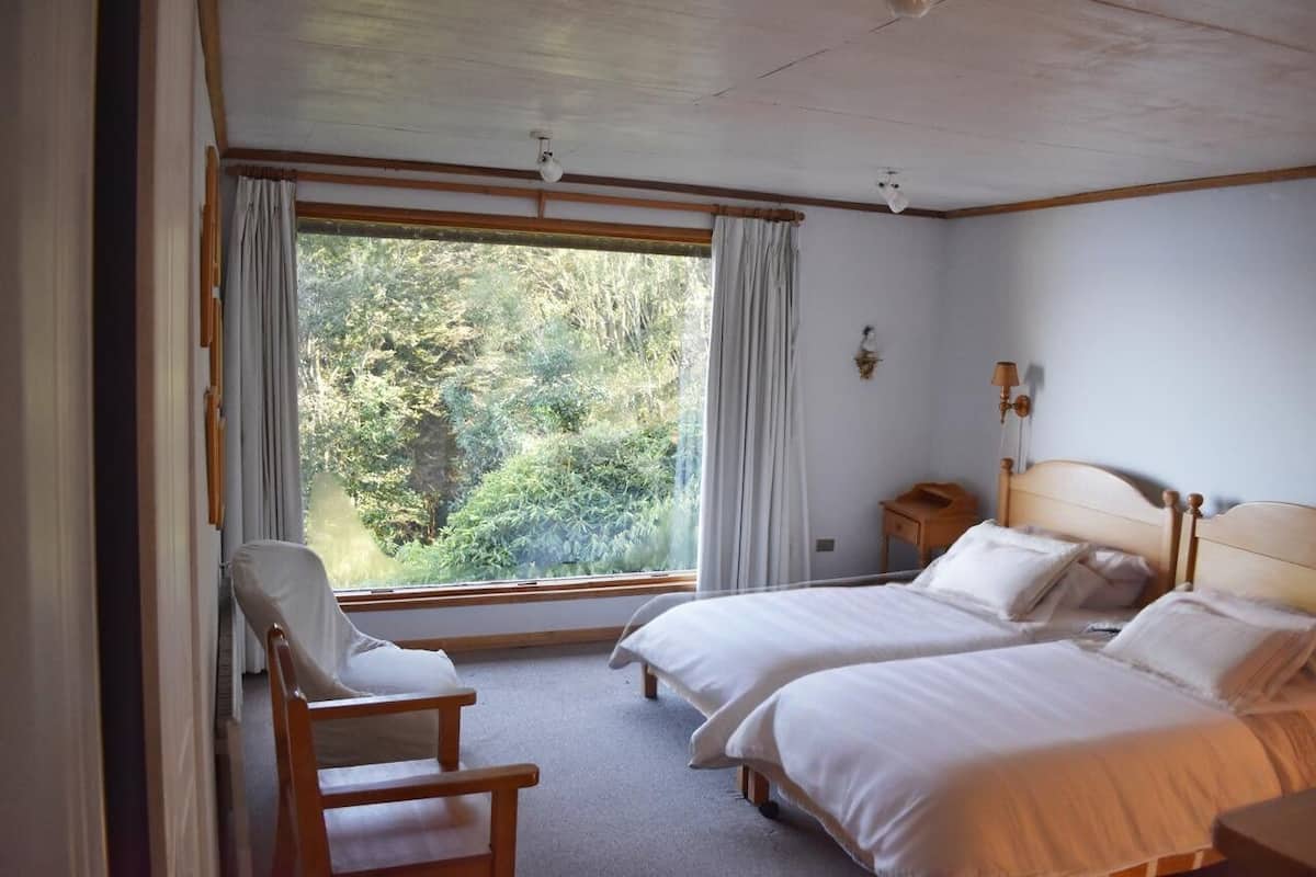 A bedroom with two beds, a chair, a nightstand, and a window with curtains.