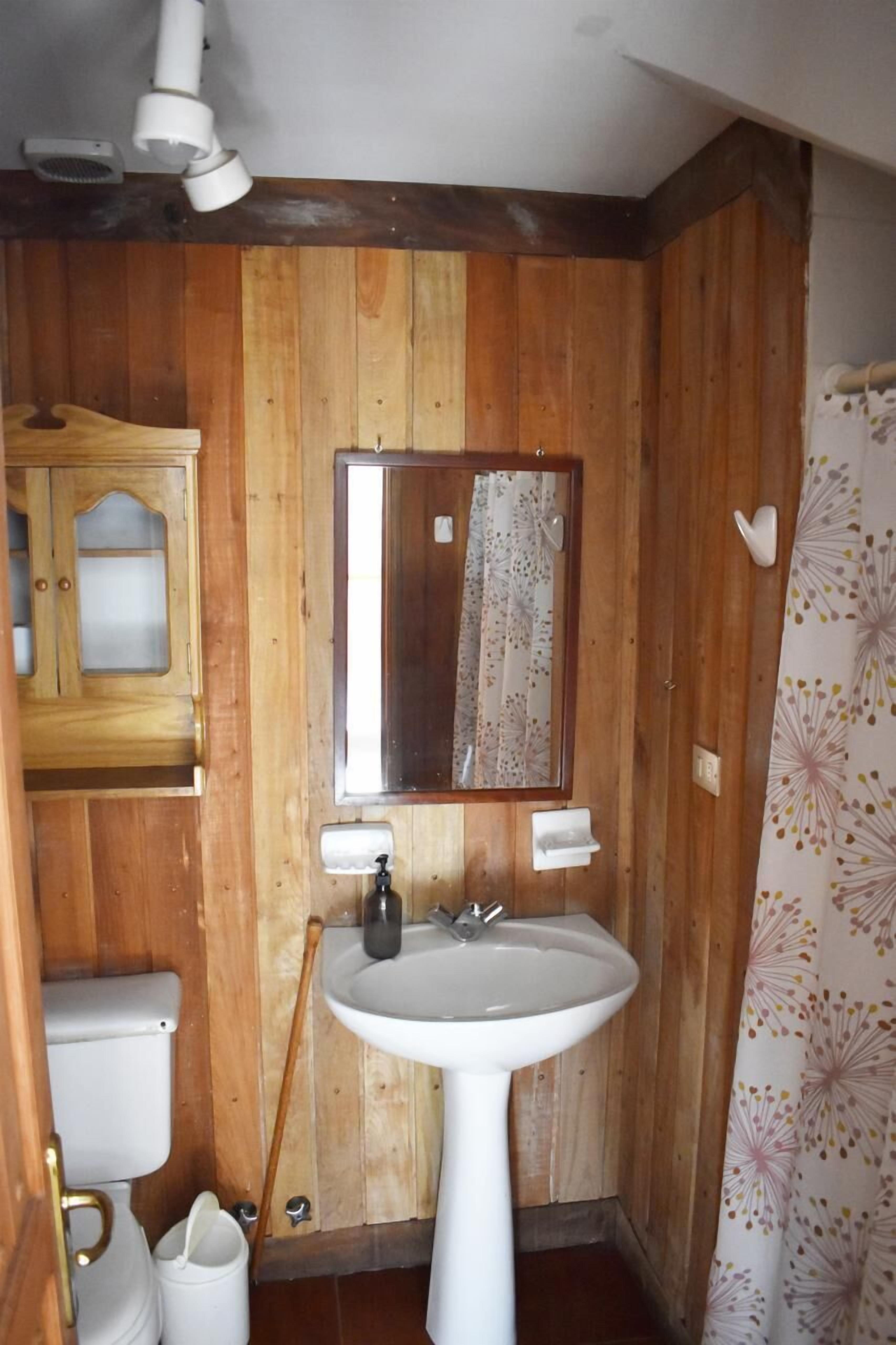 Un baño con paneles de madera, un lavamanos blanco, un espejo y un inodoro.